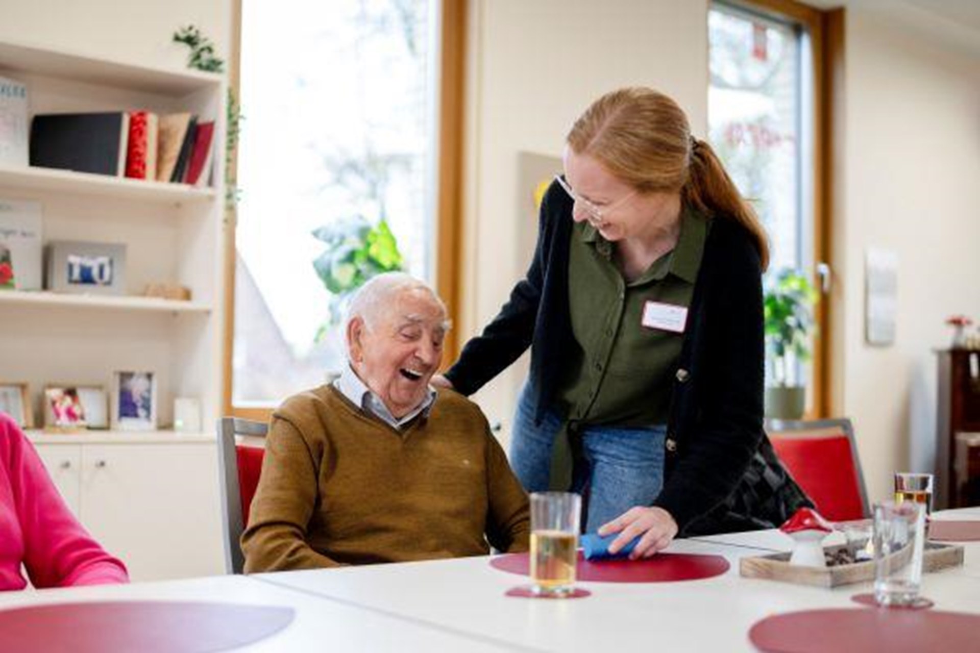 Eine Frau reicht einem Senior seine Medikamente