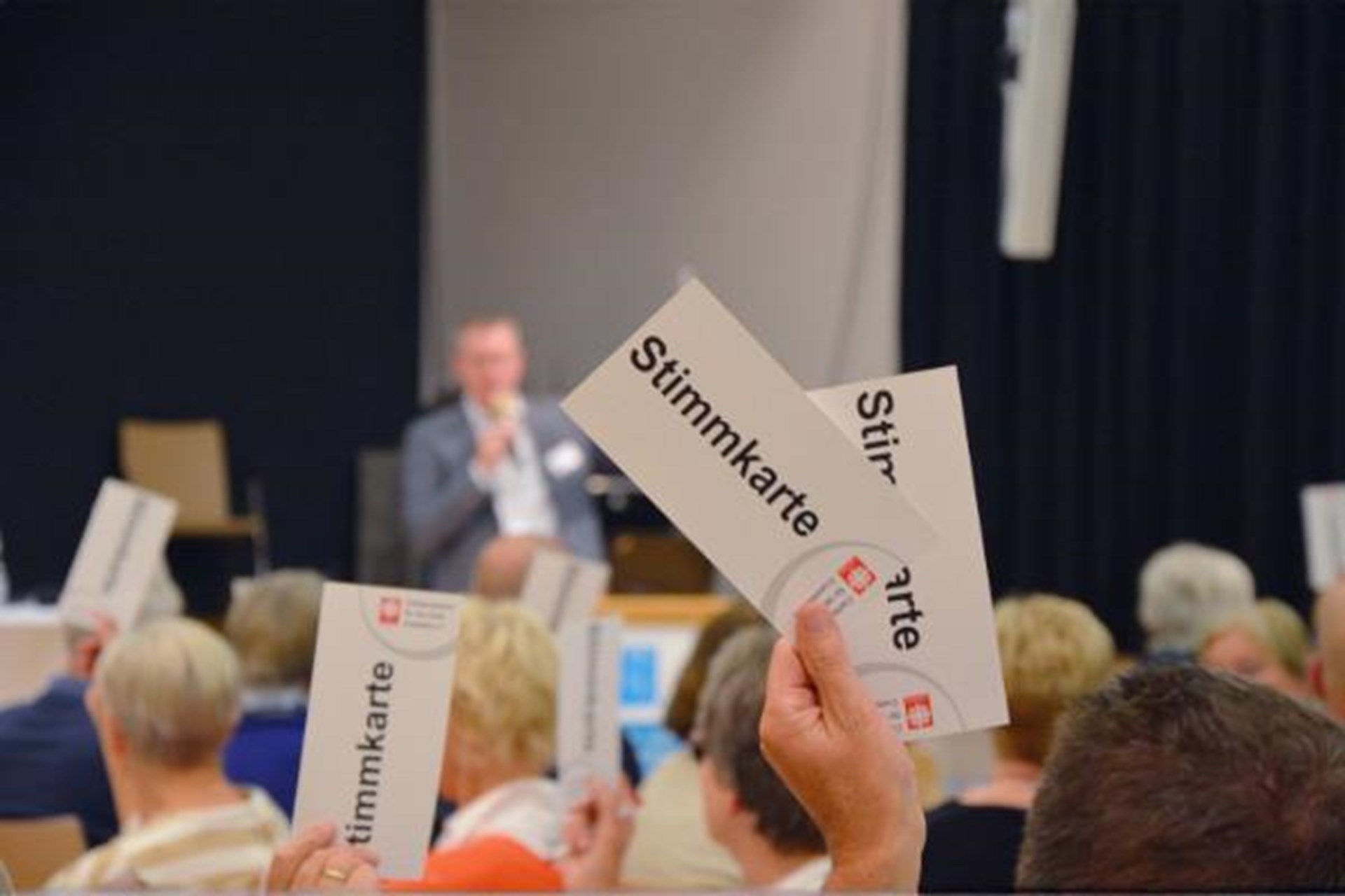 Zettel mit Aufschrift Stimmkarte wird in die Höhe gehoben