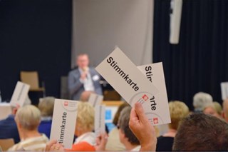 Zettel mit Aufschrift Stimmkarte wird in die Höhe gehoben