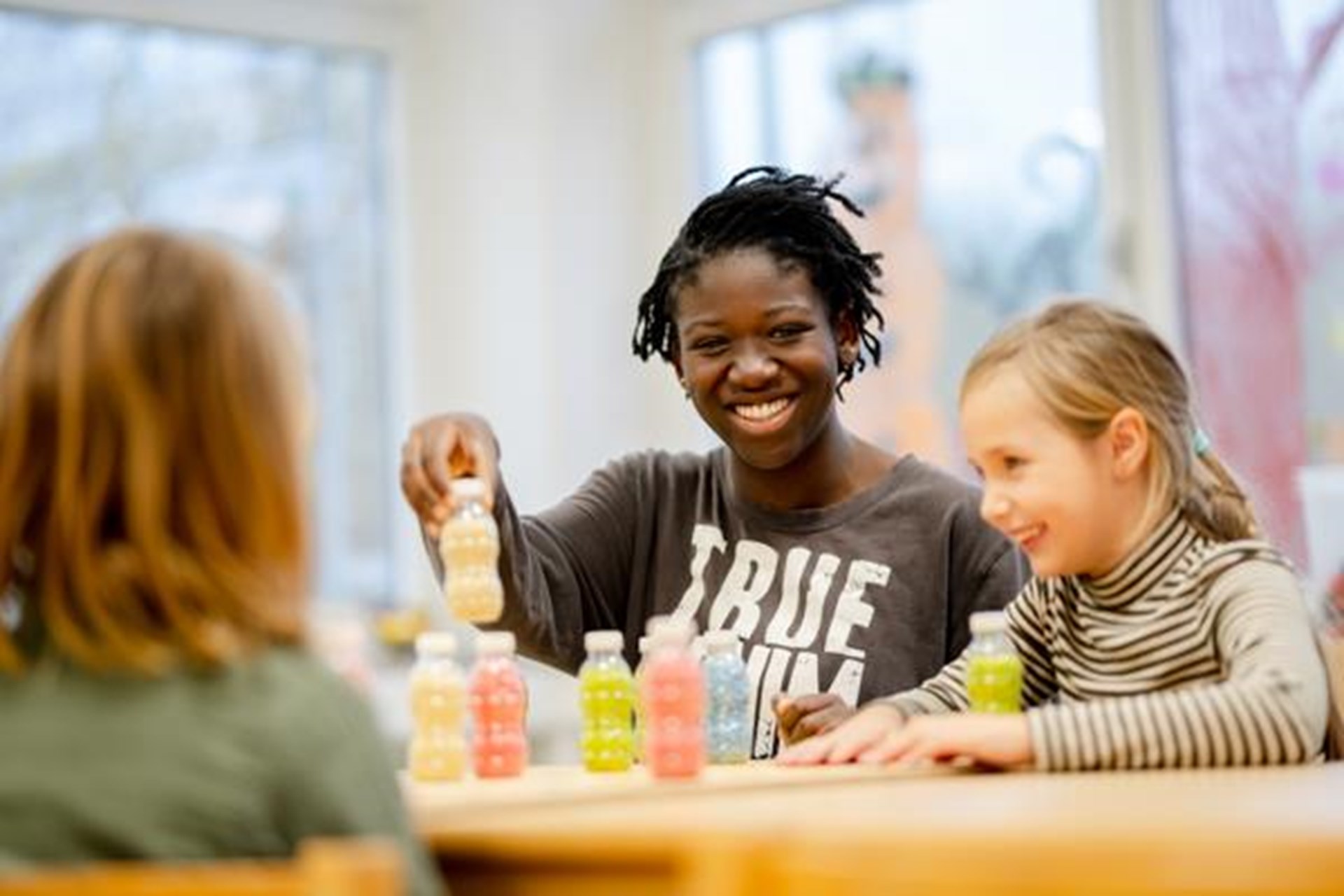 Junge Frau spielt mit Kindern am Tisch