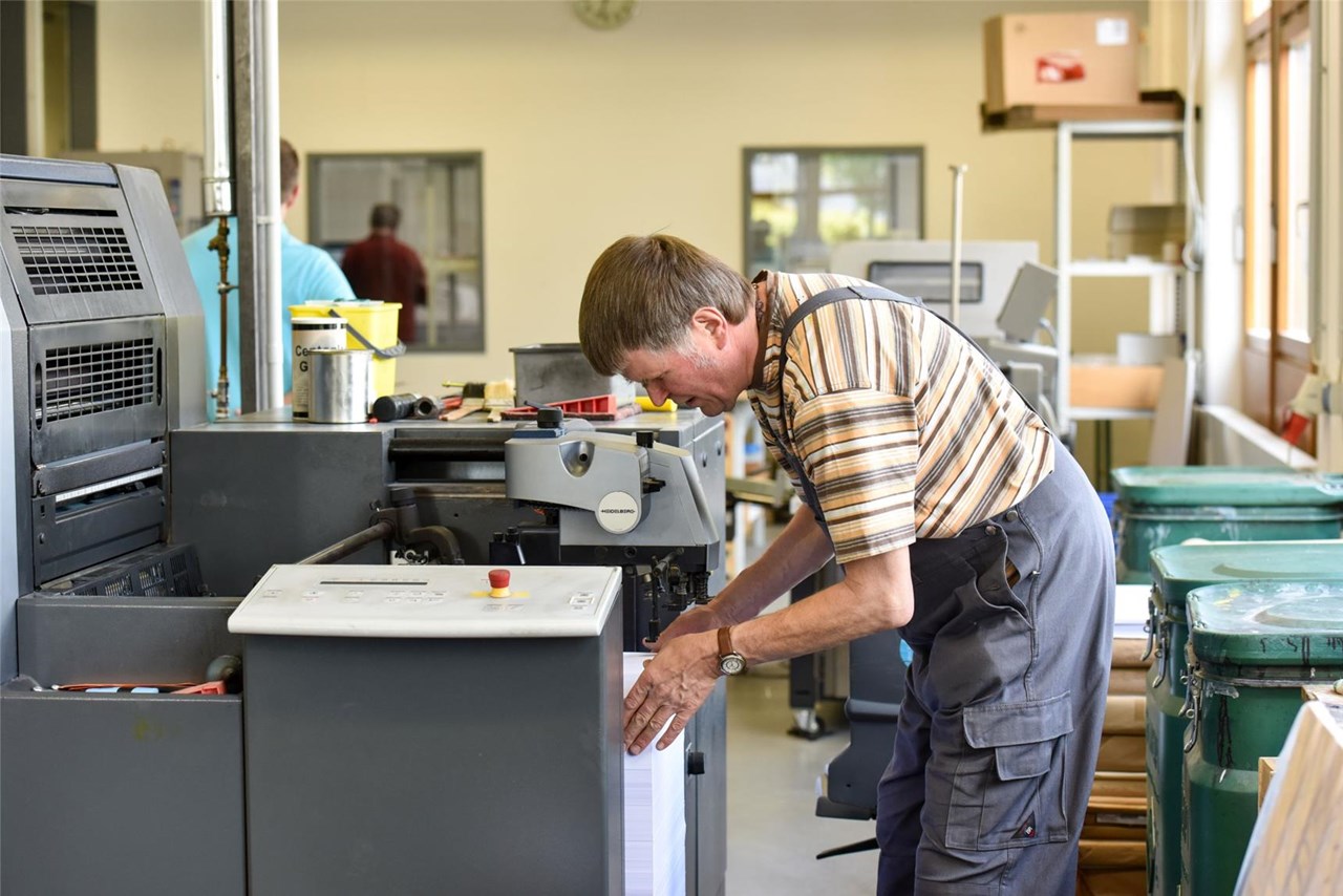 Mann mit Behinderung in Arbeitskleidung bedient eine Maschine
