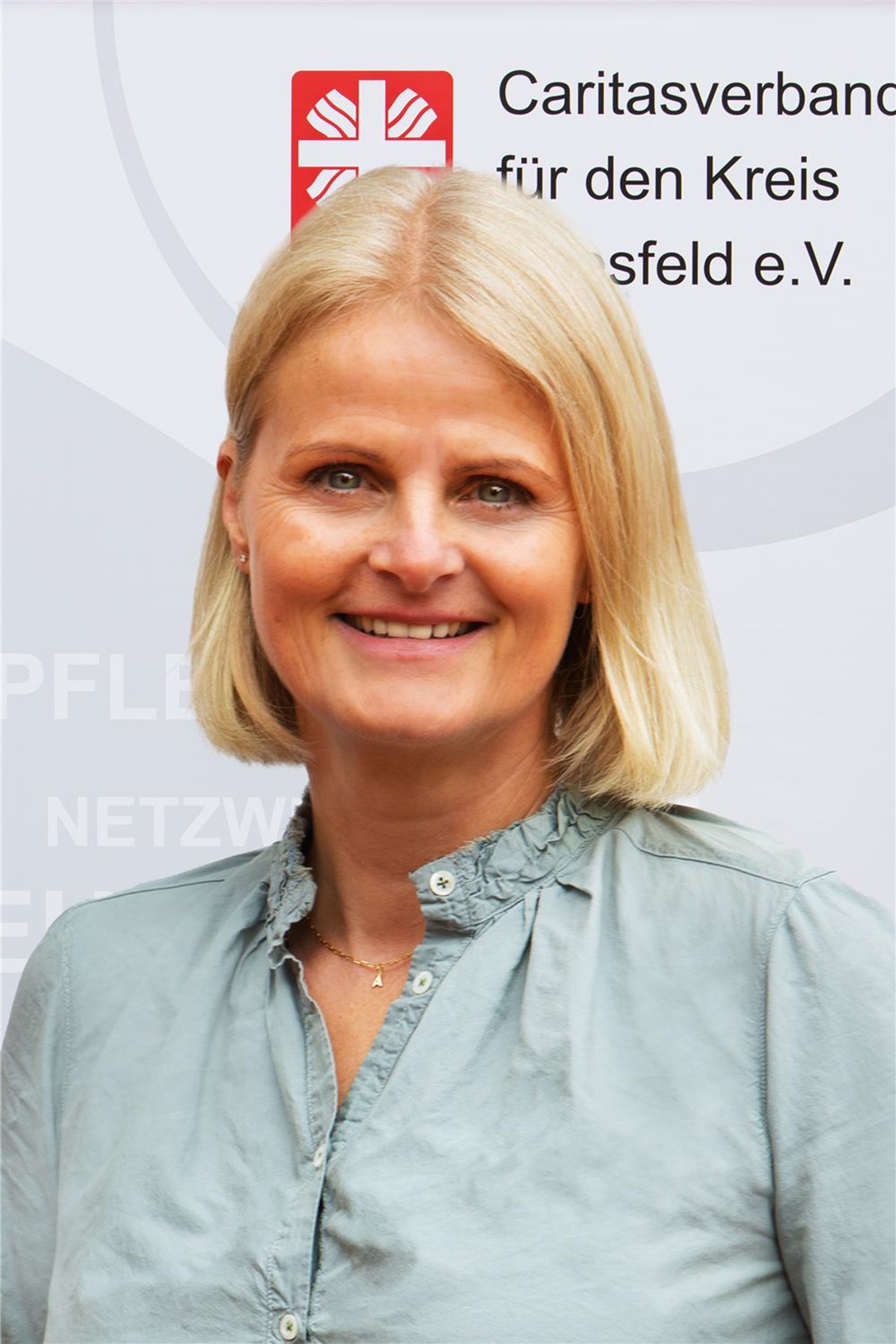 Portraitfoto von Astrid Sindermann mit Caritas-Logo im Hintergrund