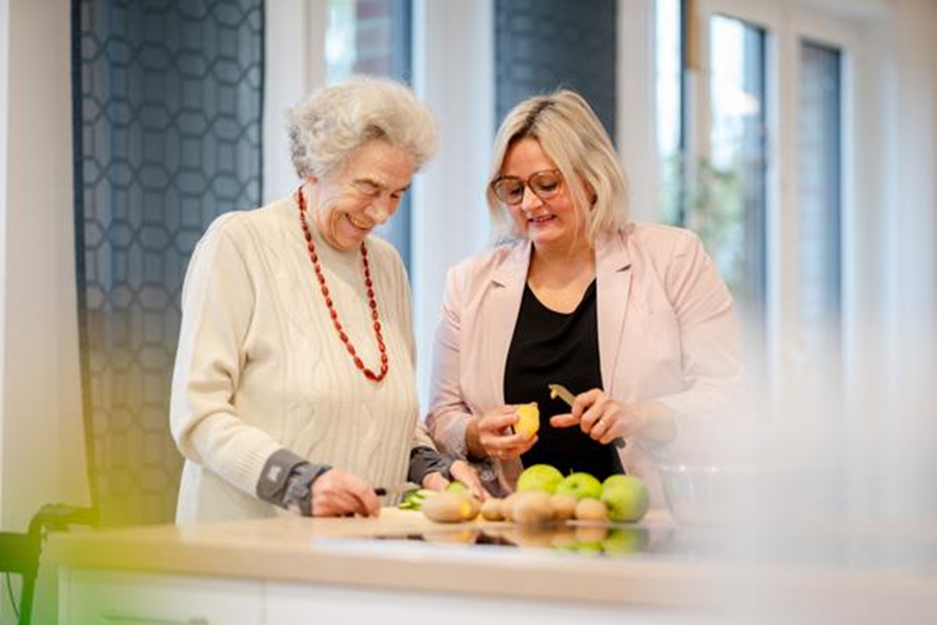 Eine Frau schält gemeinsam mit einer Seniorin Kartoffeln.
