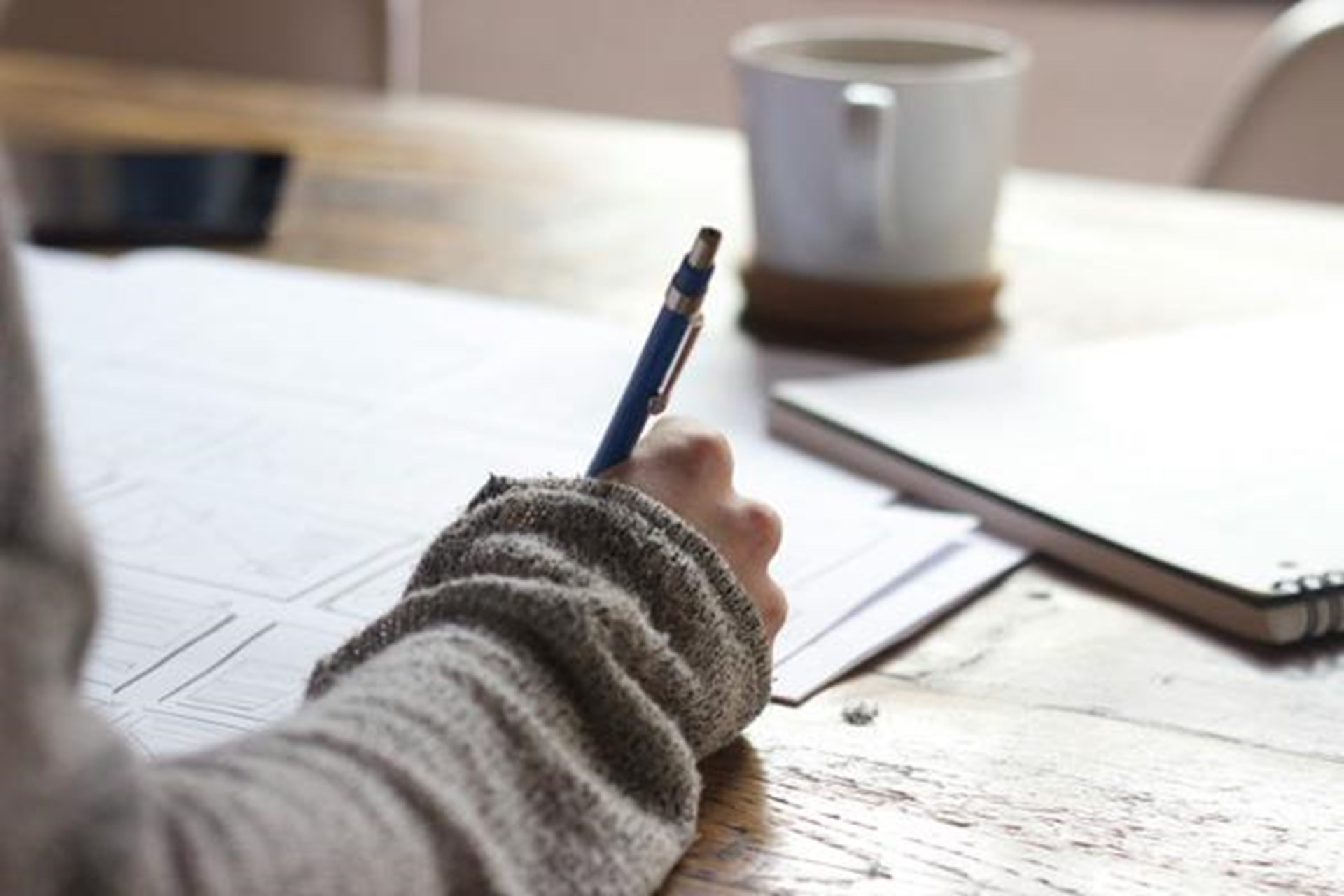 Person sitzt vor Tisch und schreibt auf Papier