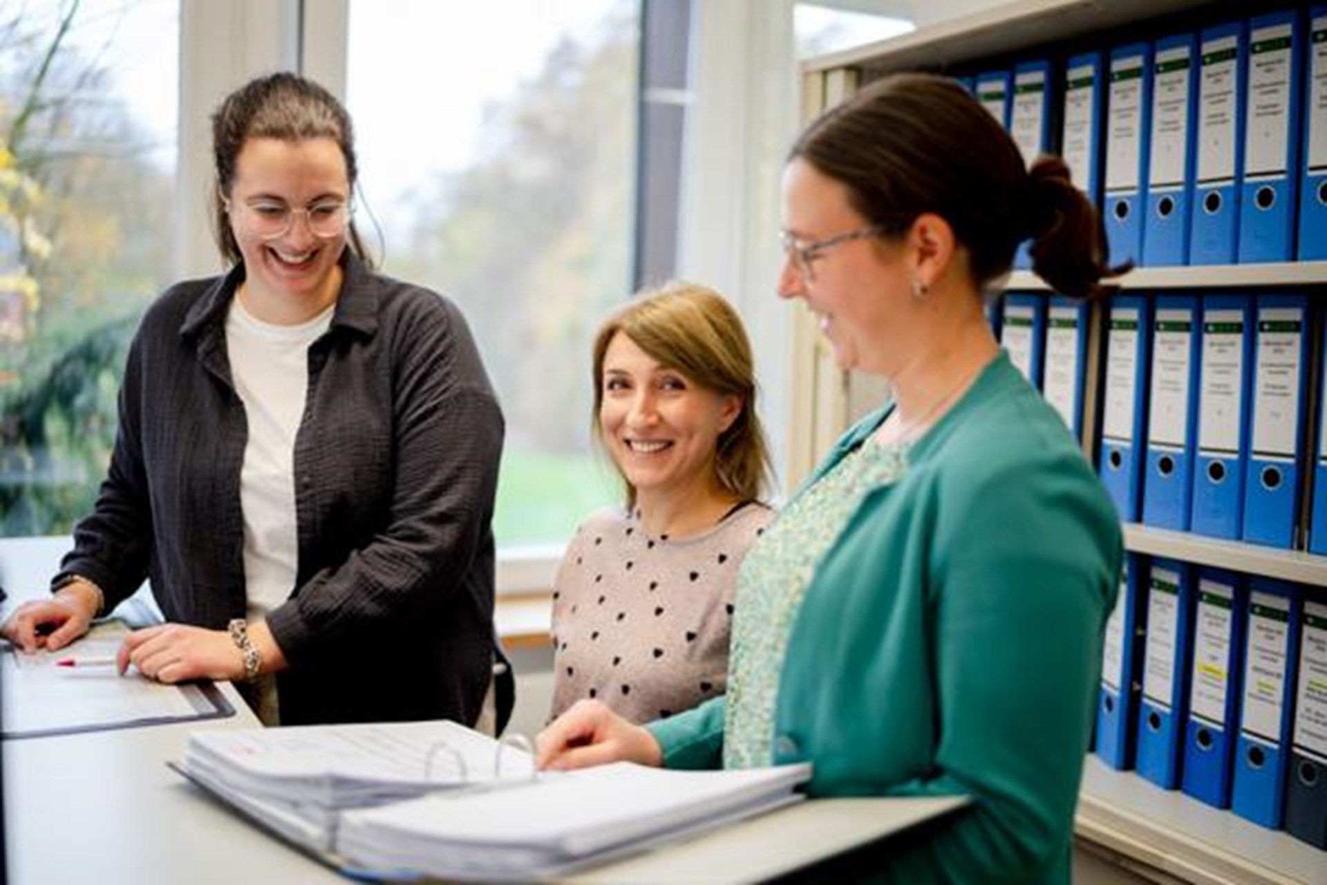 Drei Frauen stehen vor einem Tisch und schauen auf Papier